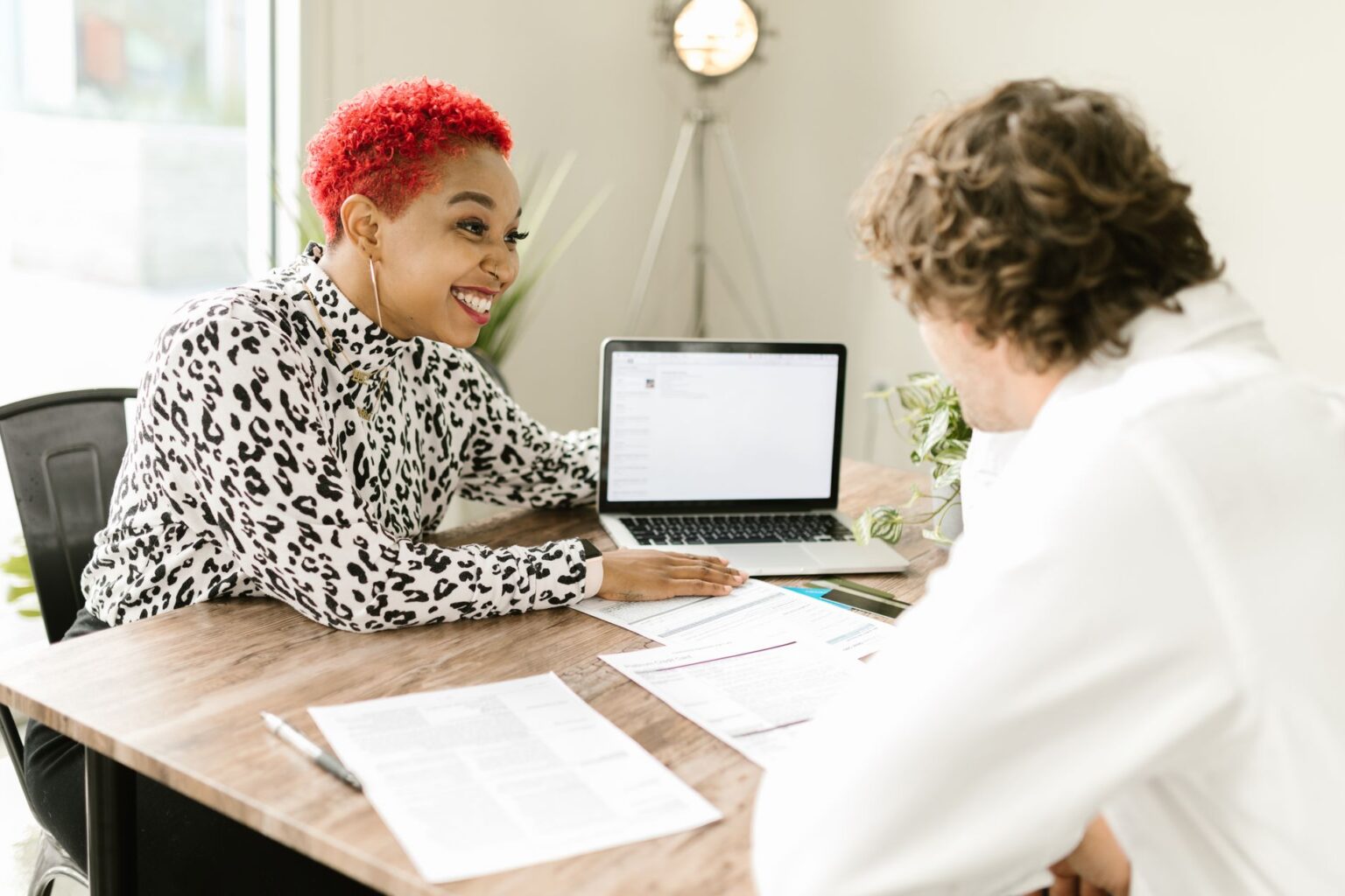 An adviser talking with a client across a table of documents and a laptop