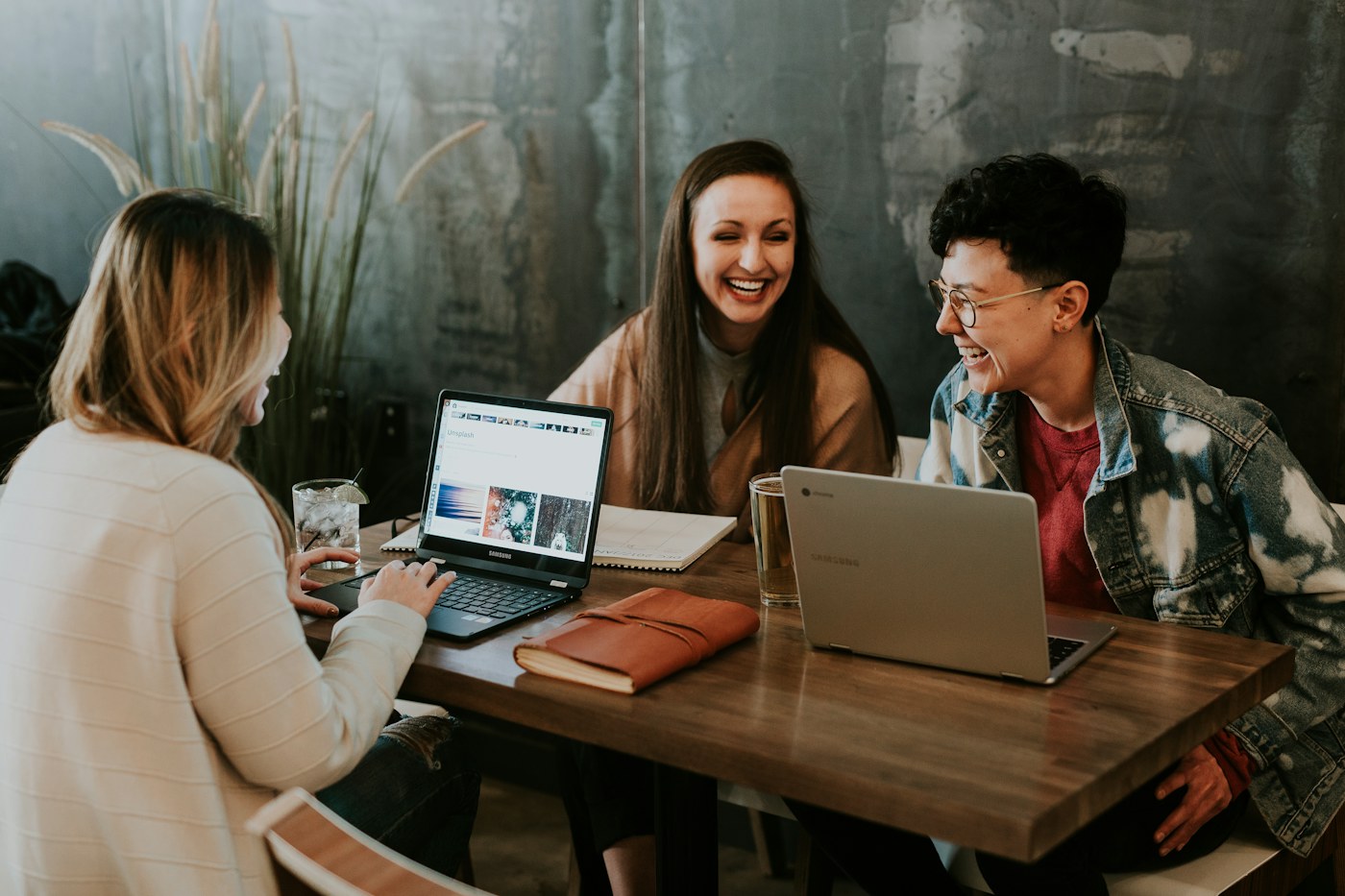 Three colleagues talking over laptops at a wooden table