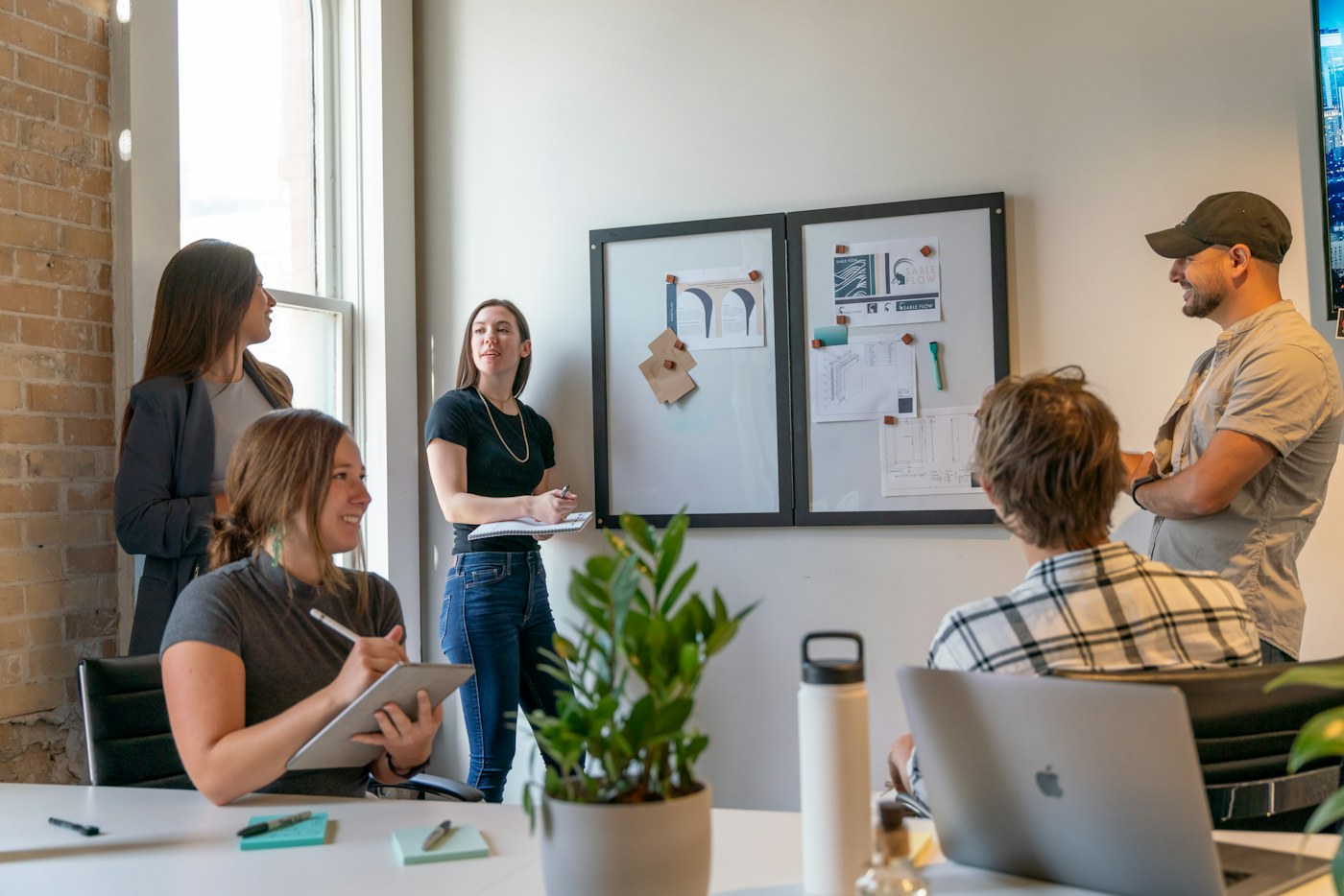 A small team discussing ideas around a pinboard in a brick-walled office