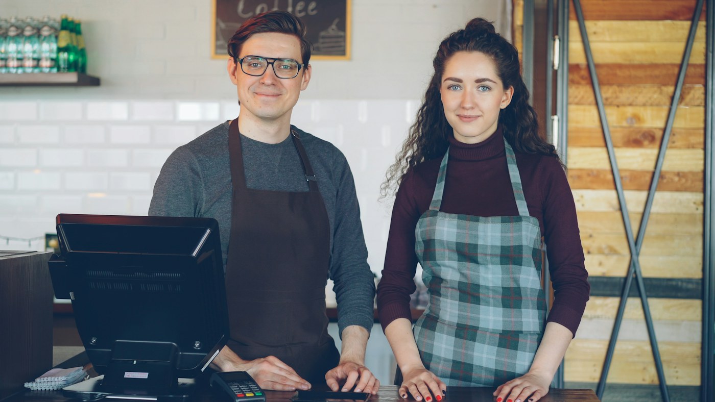 Two cafe owners in aprons standing behind their counter